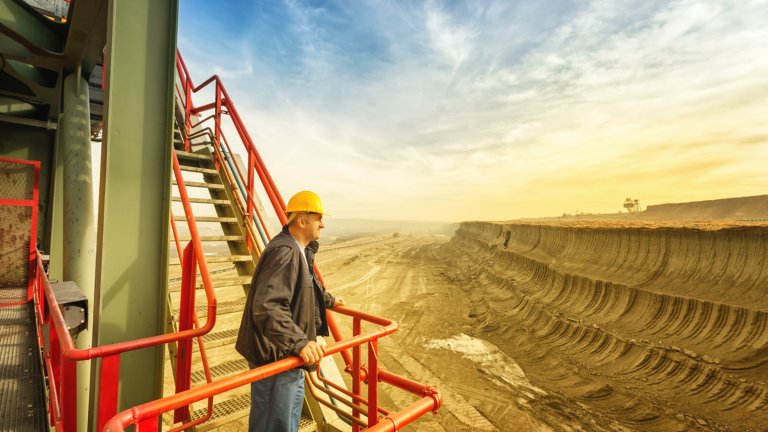 Ingénieur confiant portant un casque, se tenant sur une foreuse géante et regardant sur le côté. Site d’exploitation minière en arrière-plan