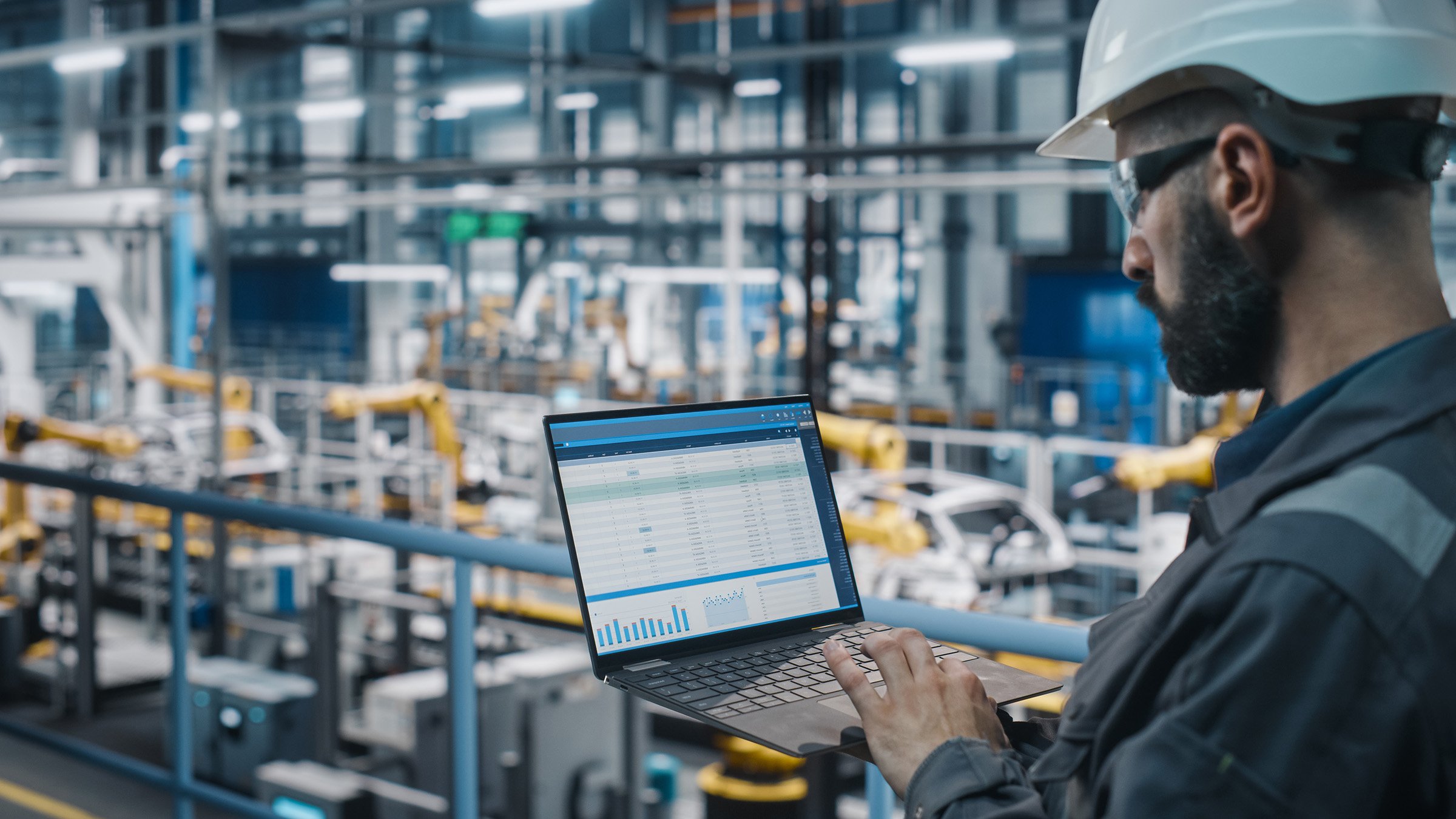 engineer in safety uniform using laptop in automotive manufacturing plant