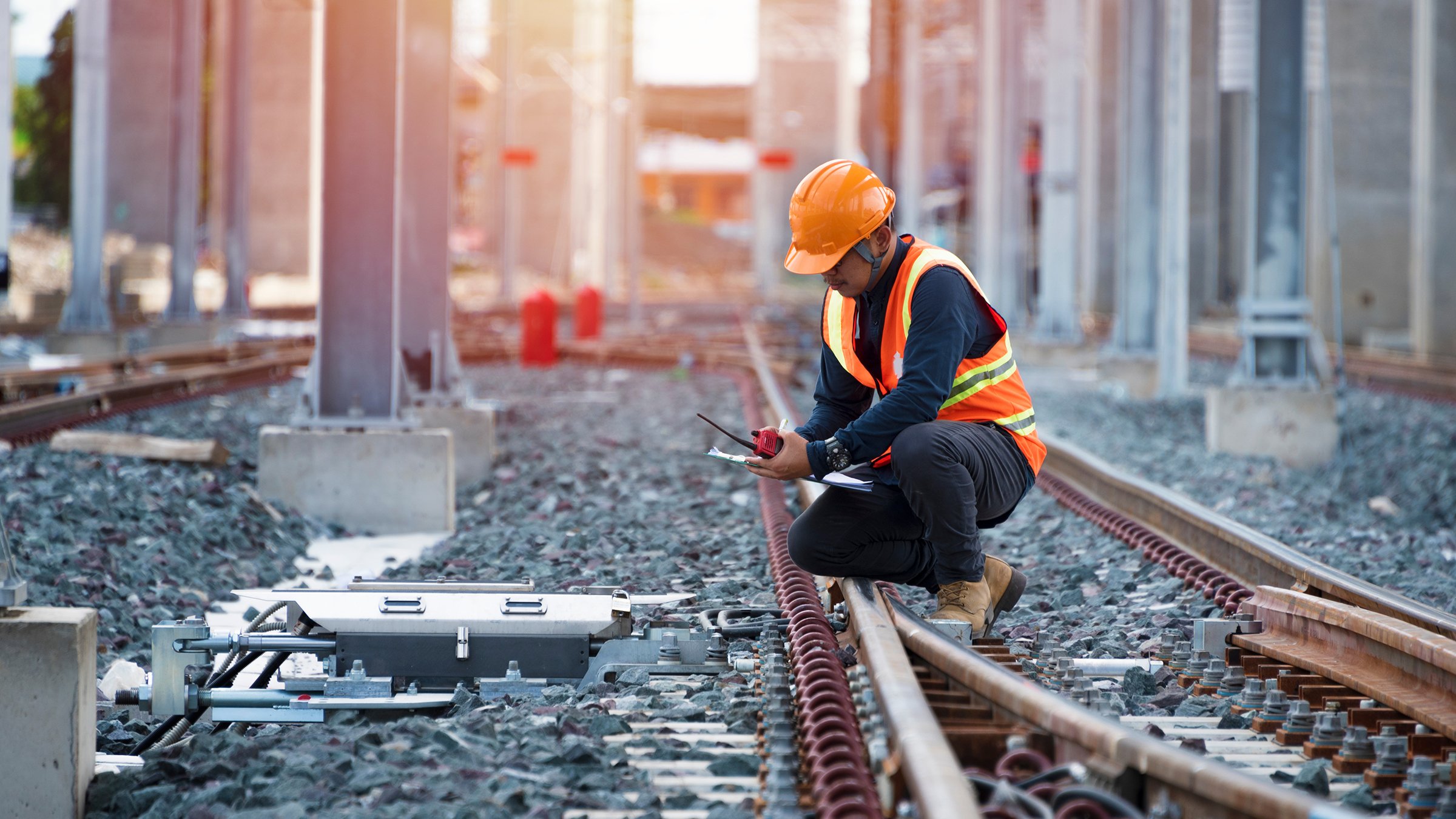 Ingénieur portant un casque et un gilet de signalisation se pose sur une voie ferroviaire pour inspecter une infrastructure critique