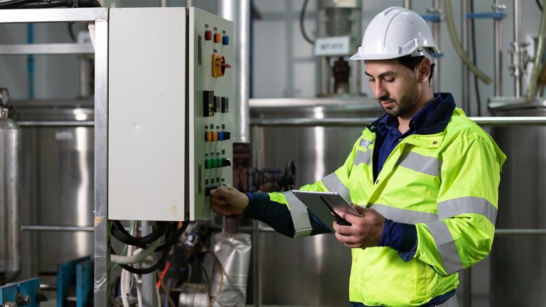 Ingénieur ou employé d’usine utilisant une tablette pour découvrir le fonctionnement d’un panneau de commande de machine dans une usine