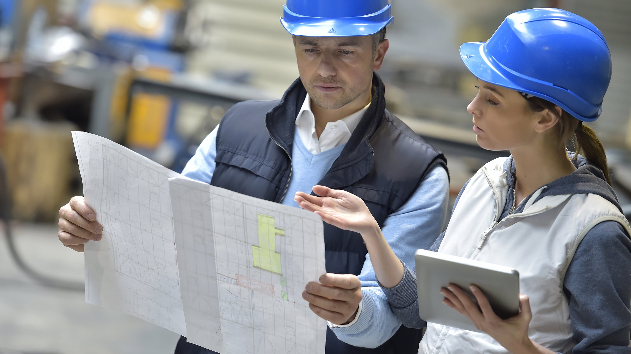 Engineers in hard hats in a manufacturing plant reading instructions.