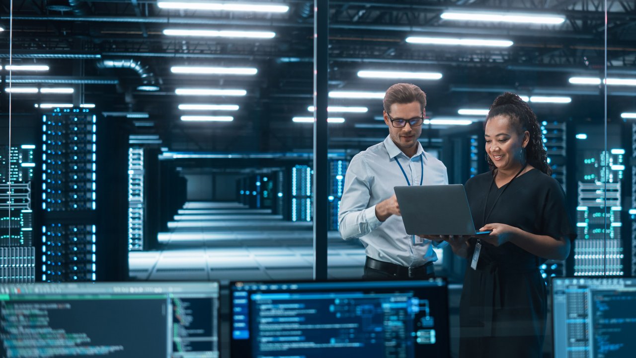 Deux ingénieurs, un homme et une femme, debout dans un centre des opérations de sécurité industrielles tiennent une tablette et surveillent la cybersécurité du réseau.