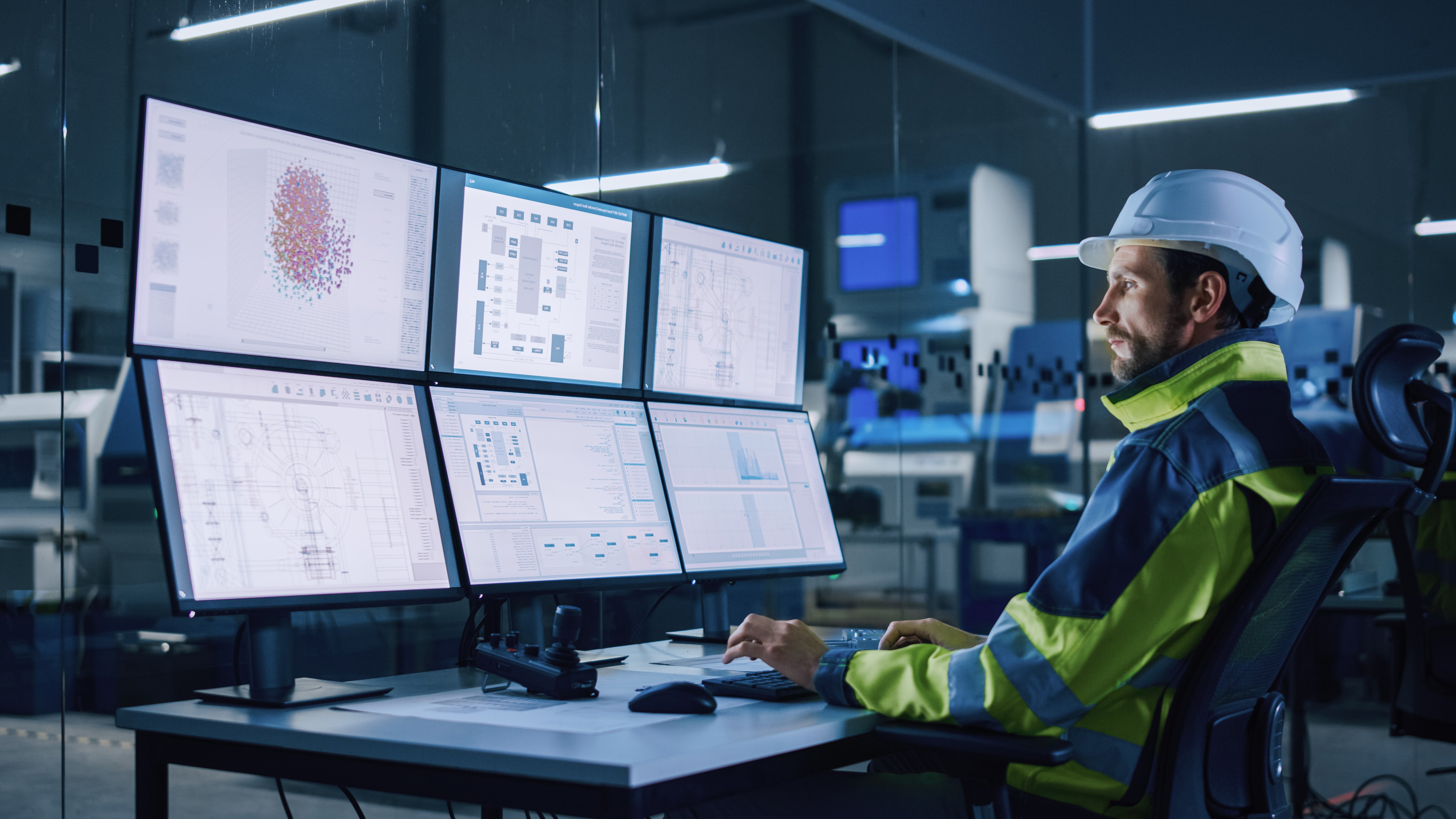 Industry 4.0 Modern Factory: Facility Operator Controls Workshop Production Line, Uses Computer with Screens Showing Complex UI of Machine Operation Processes, Controllers, Machinery Blueprints