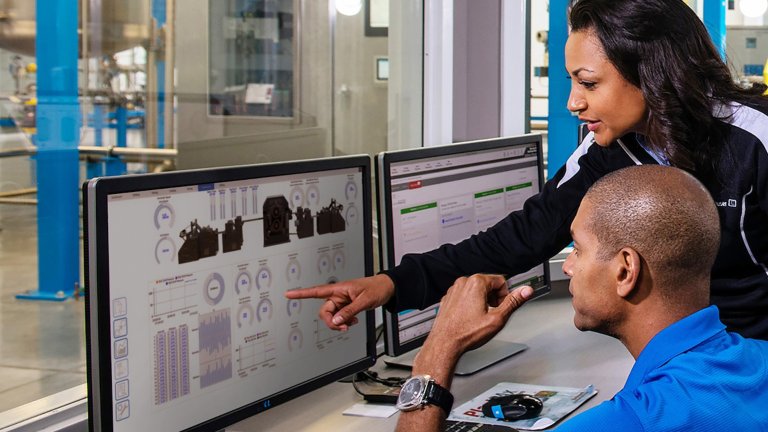 Zwei Personen schauen auf einen Bildschirm mit der FactoryTalk Optix-Software. Einer gestikuliert auf den Bildschirm, während sie zusammenarbeiten.