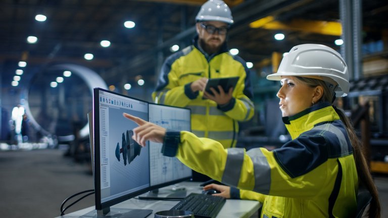 Ingeniera con chaqueta amarilla apuntando al monitor en las instalaciones de producción
