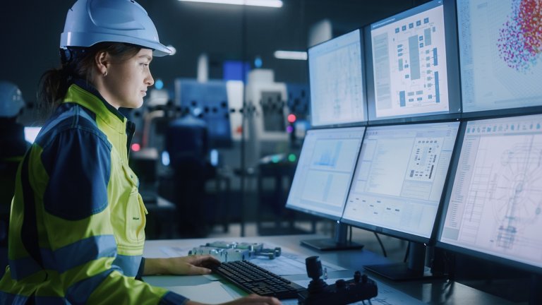 Industry 4.0 Modern Factory: Female Facility Operator Controls Workshop Production Line, Uses Computer with Screens Showing Complex UI of Machine Operation Processes, Controllers, Machinery Blueprints