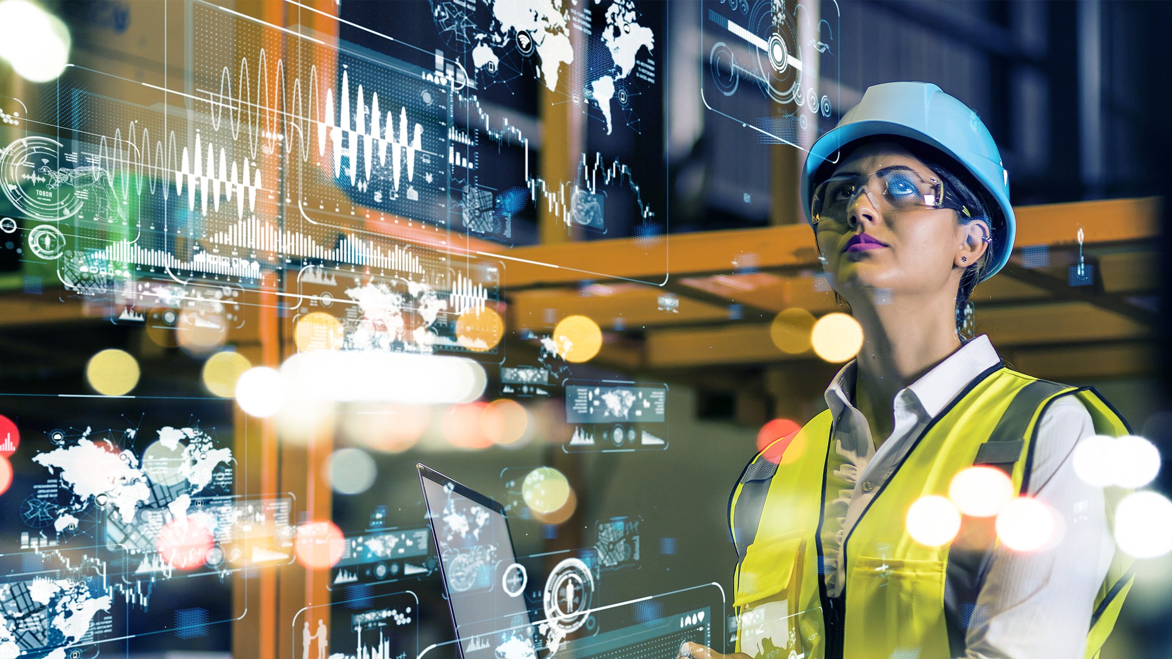 female worker in a yellow vest and a hard hat wearing safety glasses on a manufacturing plant floor