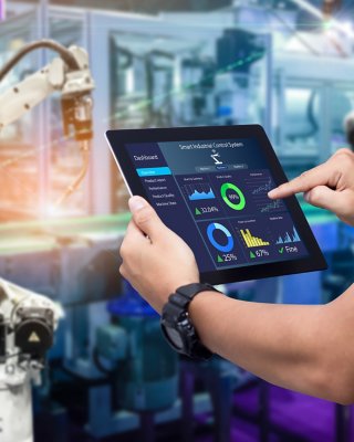 Close up view of technician’s hands holding a tablet showing analytics in a factory in front of white robotic arm.
