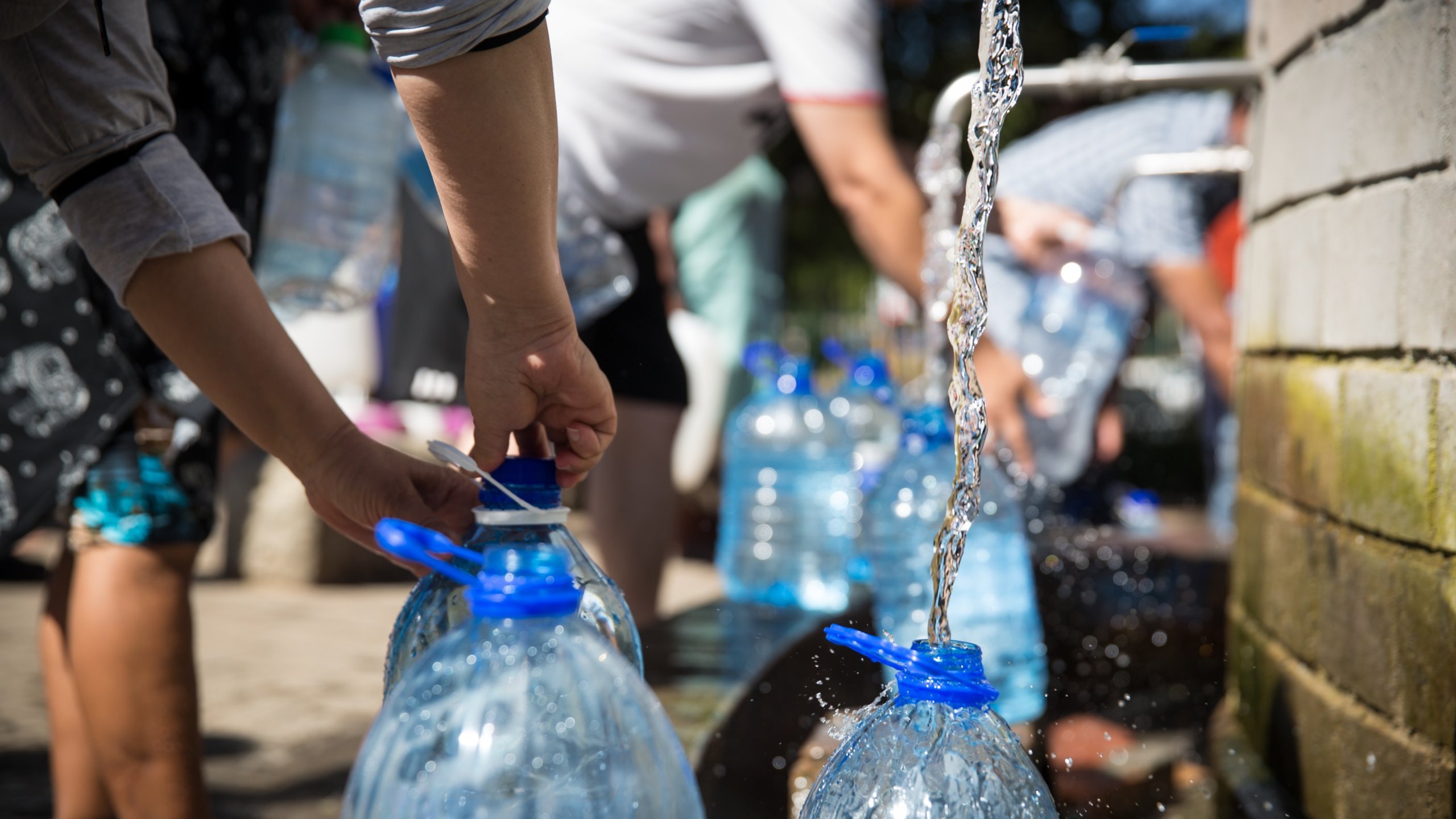 people pouring tap water into large plastic bottles