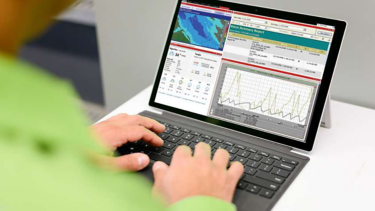 Individual engaged with a laptop, reviewing a weather forecast displayed on the screen.