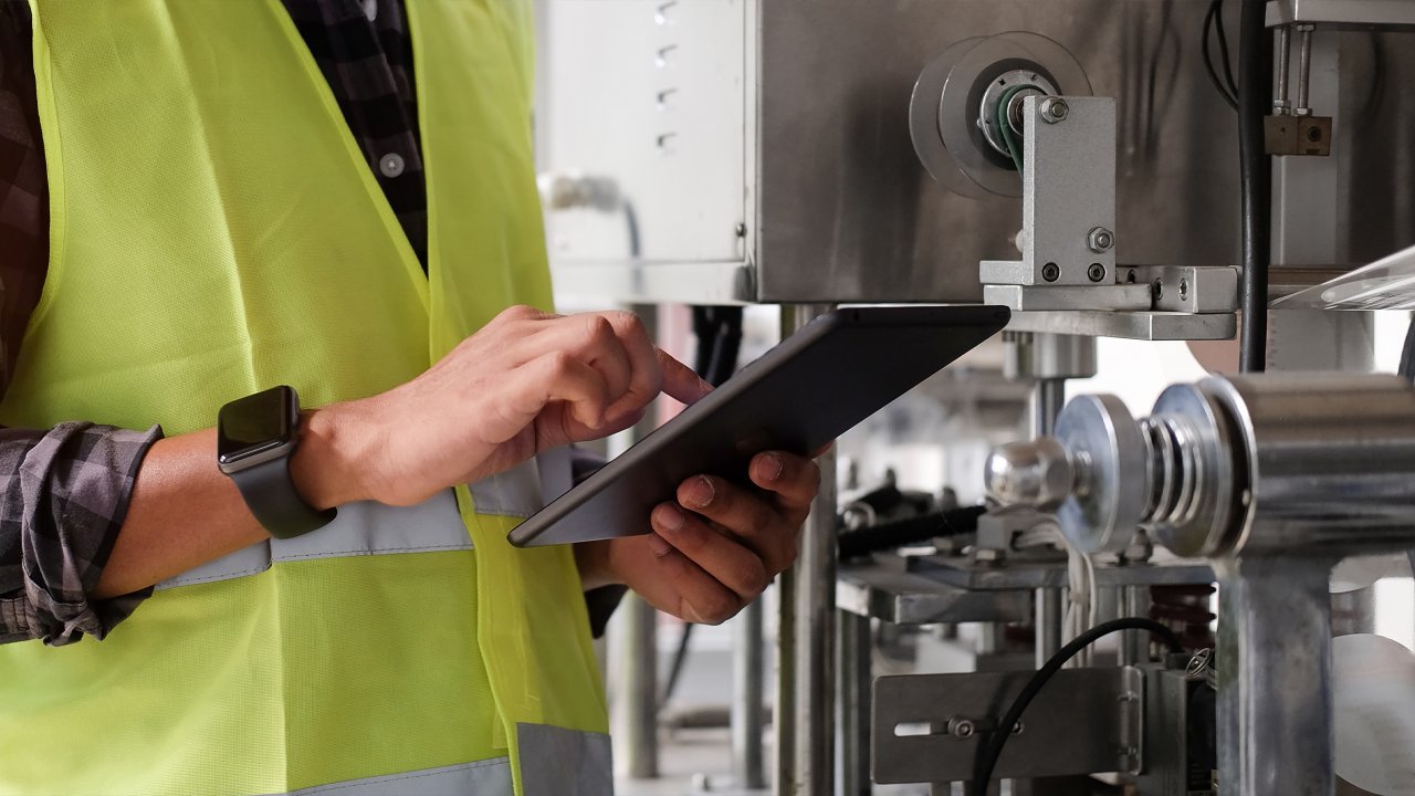 Industrial Engineer in yellow vest working and monitoring system software on a tablet