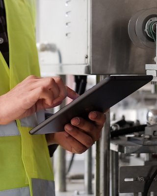 Industrial Engineer in yellow vest working and monitoring system software on a tablet