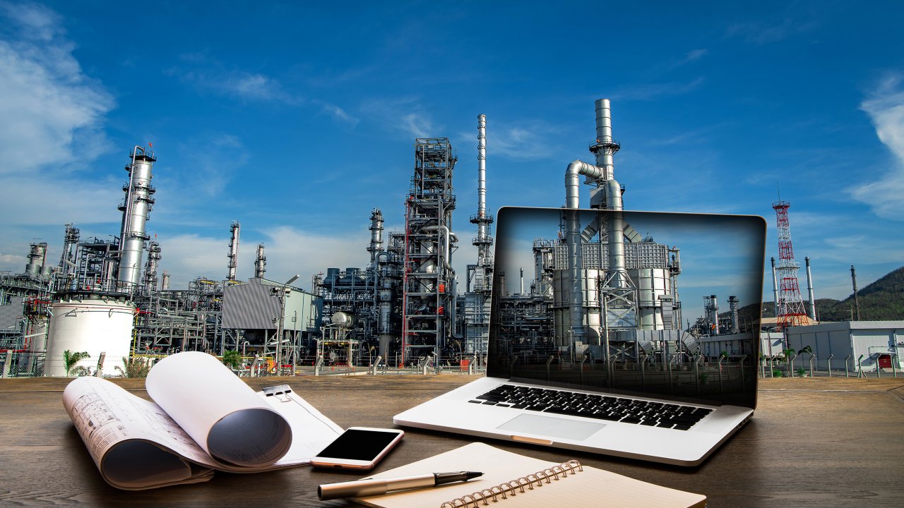 工程行业概念，桌上放着笔记本电脑和图纸，背景是石油化工厂