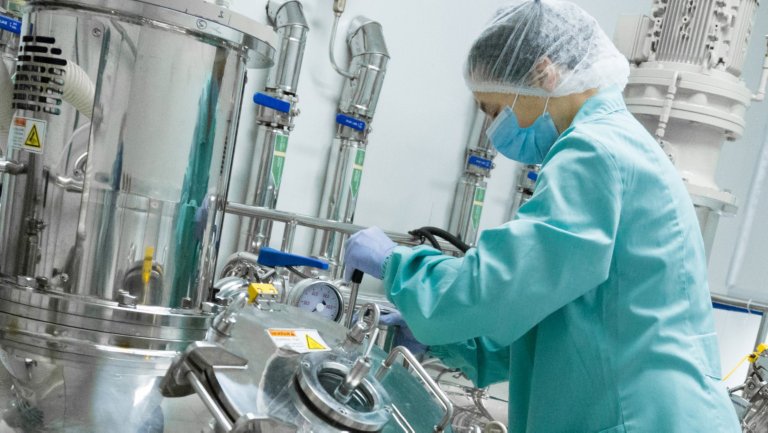 A pharmaceutical factory worker in protective clothing operates a piece of equipment on the production line.