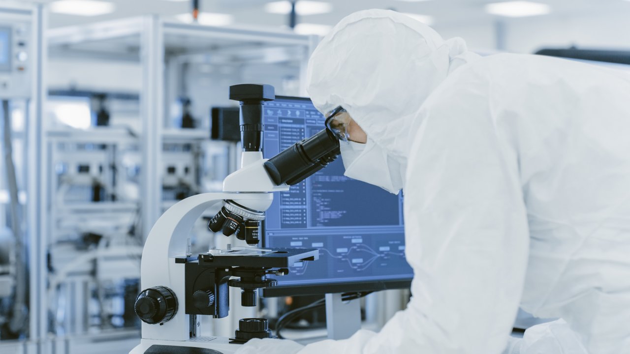 Person in white overalls loking in microscope in lab