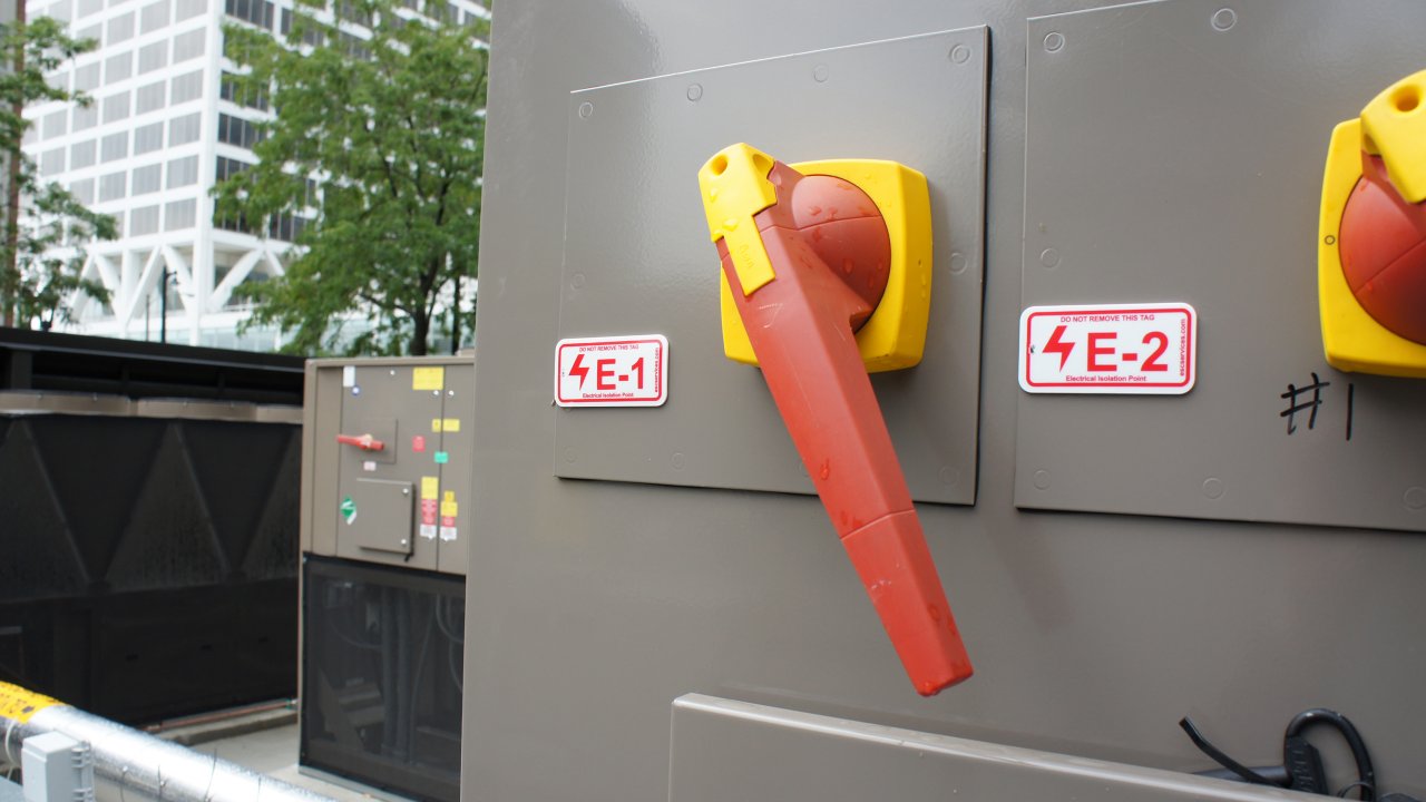 Red lockout/tagout tags for electrical sources on large gray equipment panel are important to take into account when creating LOTO procedures so maintenance employees are safe when servicing equipment.