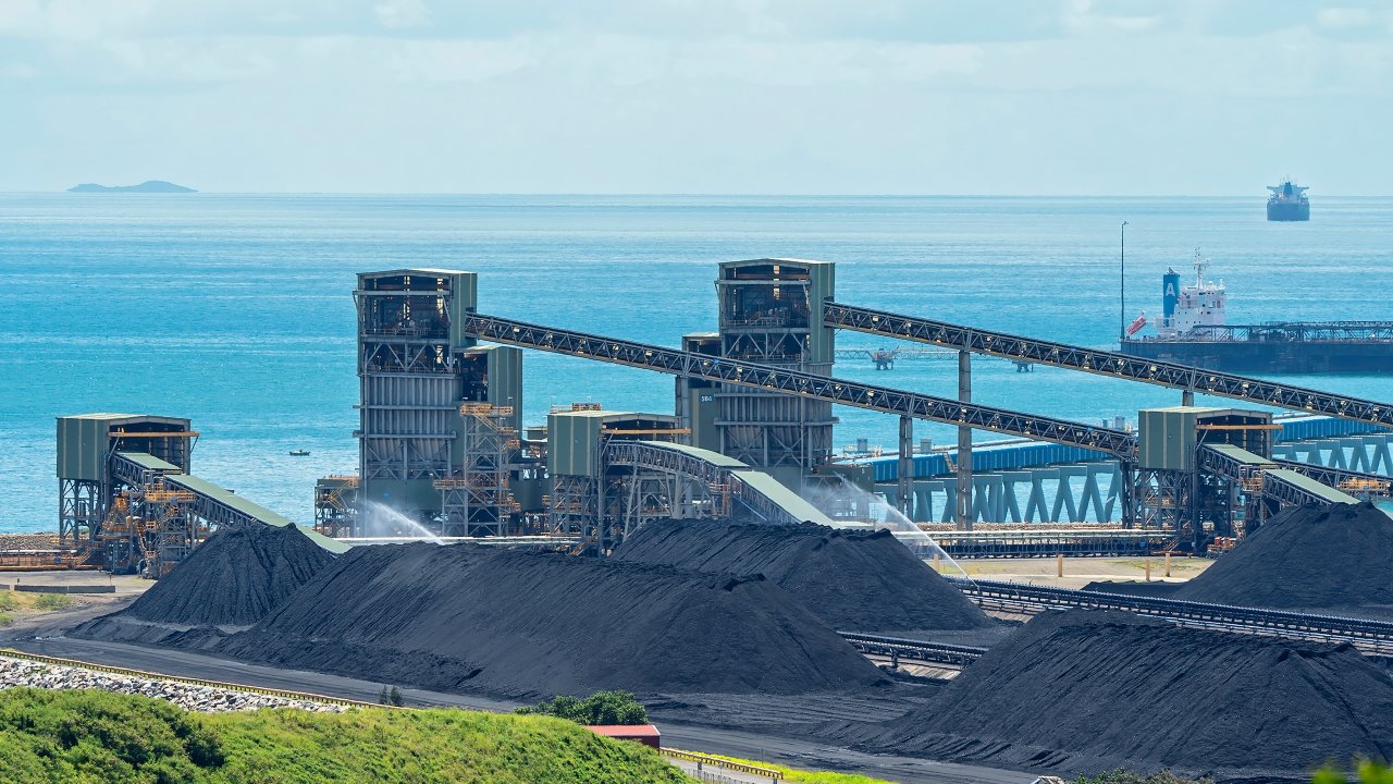 Mining operations near a port on a bright day with water in the background. Mackay, Queensland, Australia - March 2021: Port of Hay Point terminal exporting thermal and metallurgical coal from Central Queenslandâ€™s Bowen Basin mines to ports around the world.