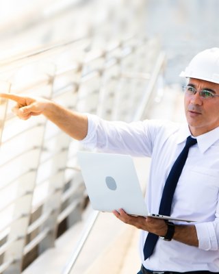 Male engineer holding laptop beside female engineer and pointing at window