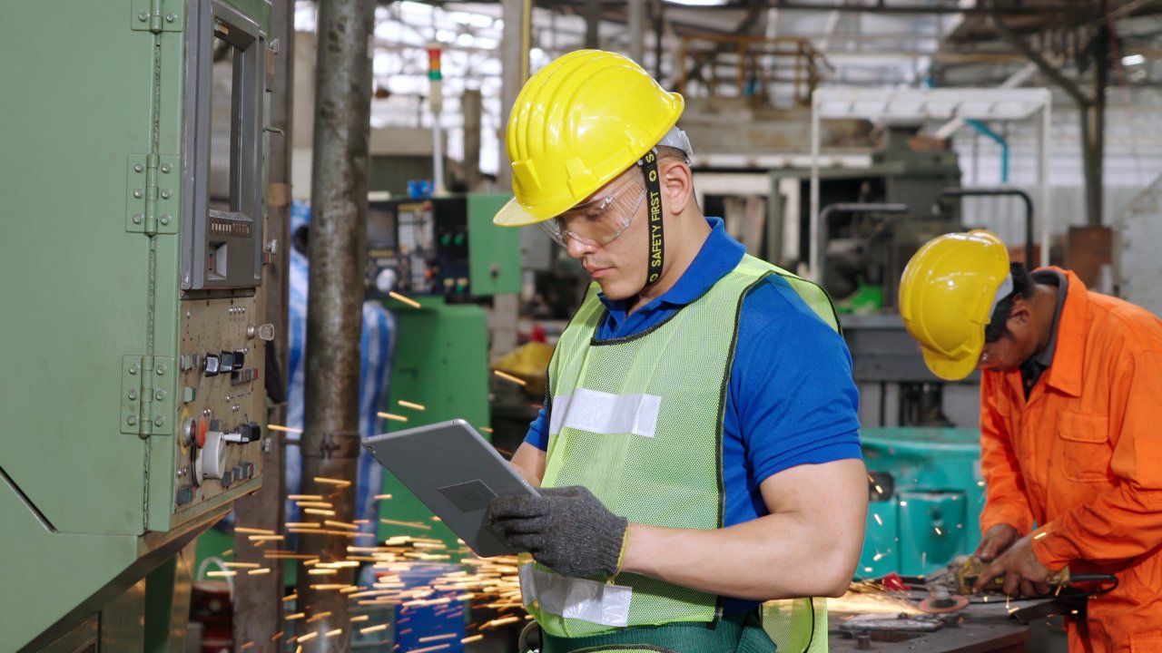 Worker wearing safety gear using a tablet to monitor control panel. Smart factory worker using machine in factory workshop . Industry and engineering concept.