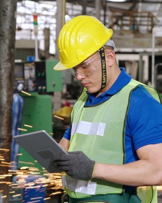 Worker wearing safety gear using a tablet to monitor control panel. Smart factory worker using machine in factory workshop . Industry and engineering concept.