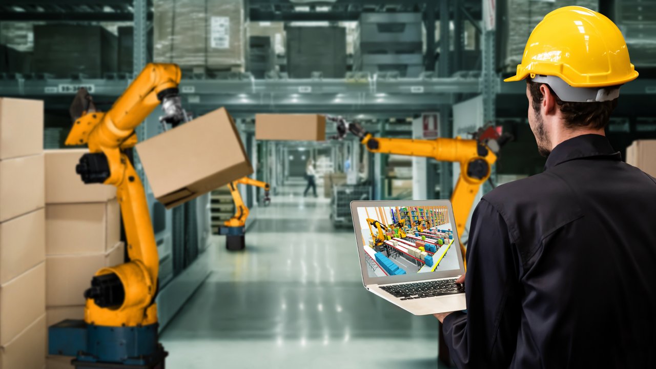 Male worker in warehouse reviewing Emulate3D simulation on laptop screen.