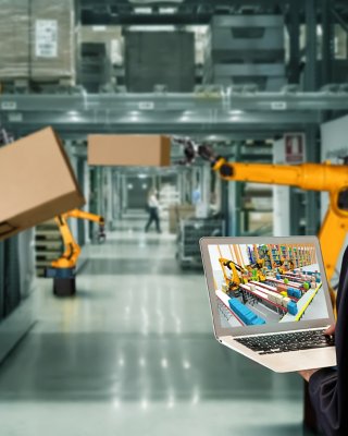 Male worker in warehouse reviewing Emulate3D simulation on laptop screen.