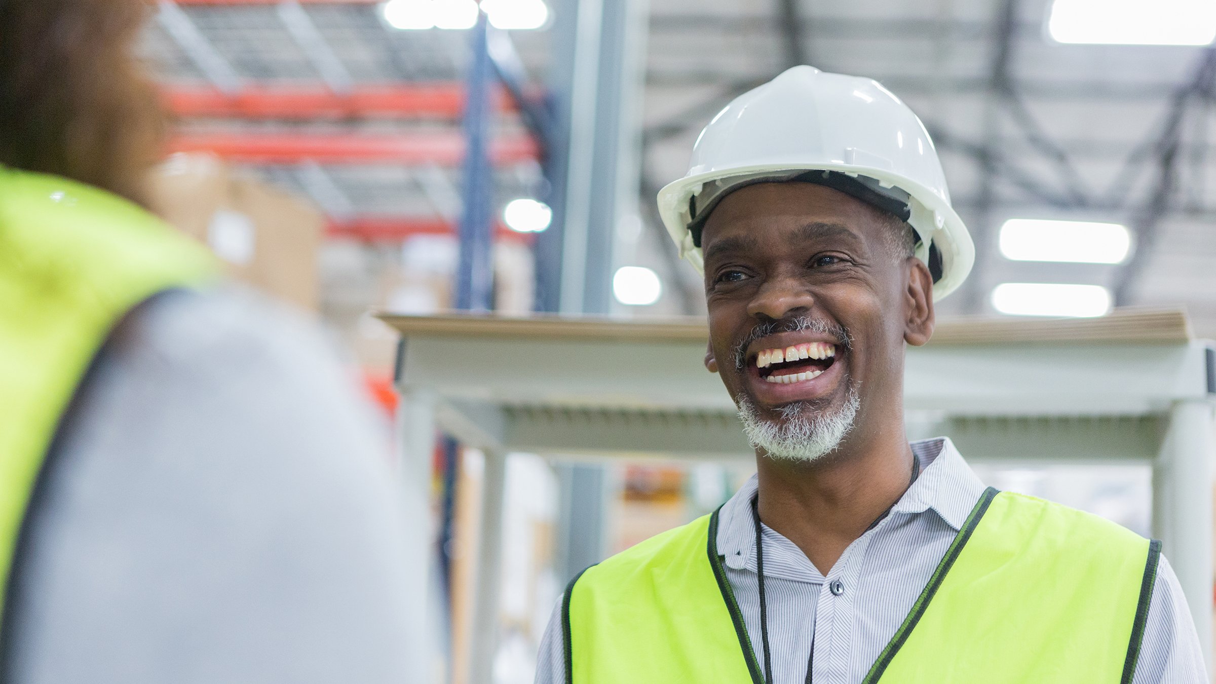 Employé souriant portant un gilet de sécurité jaune et un casque de protection blanc dans une usine