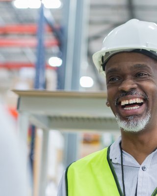 Smiling male worker wearing a yellow safety vest and a white hard hat in a plant