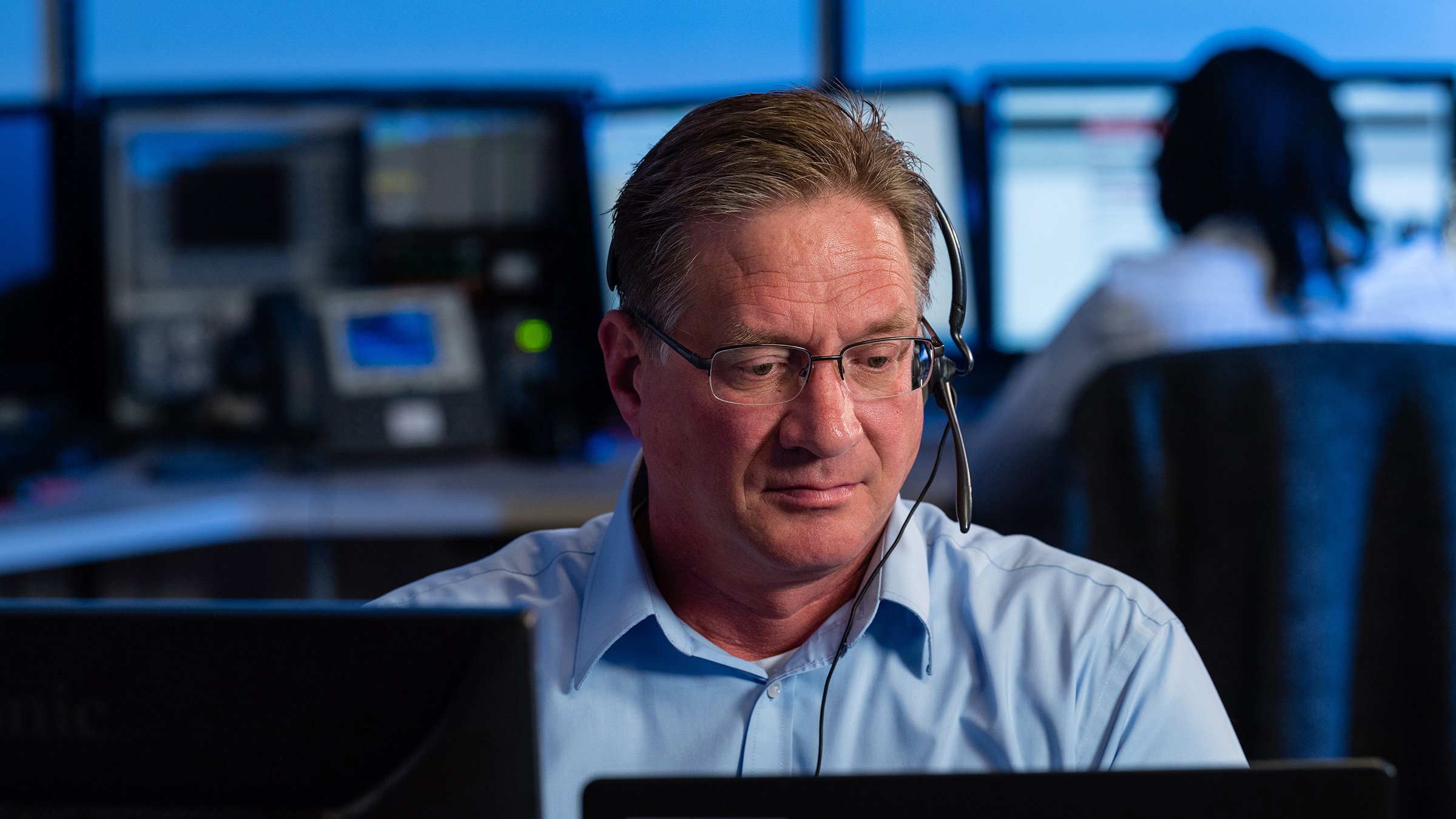 A man with a headset in a customer support office looking down at his computer.