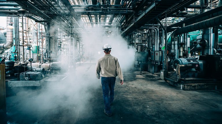 A man in a hard hat walking through a smoky manufacturing plant floor