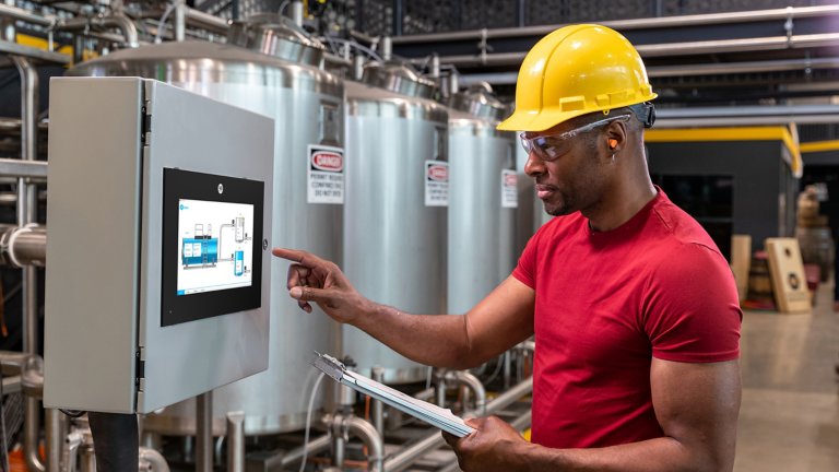 Man wearing hard hat and safety glasses on factory floor using a touchscreen on the OptixPanel Compact graphic terminal.
