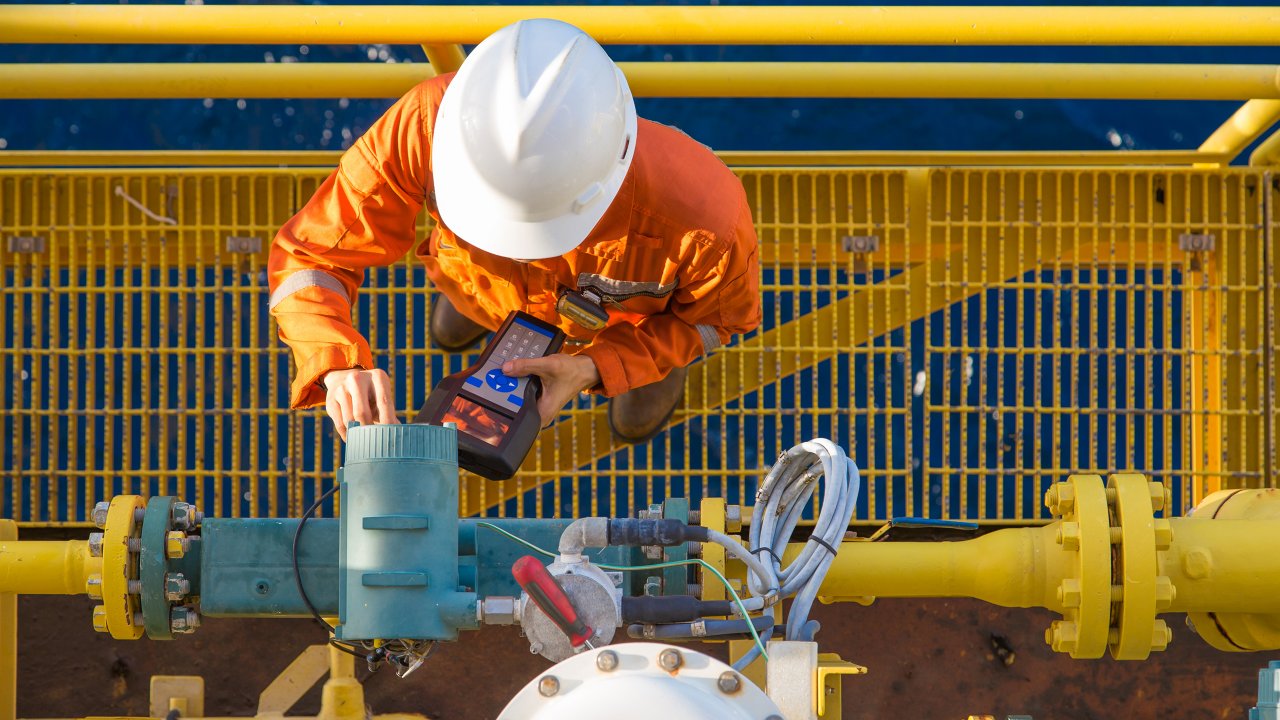 Offshore oil rig worker calibrating coriolis digital flow meter by using hand held communicator to connect between devices, instrument and electrical service of oil and gas energy business.
