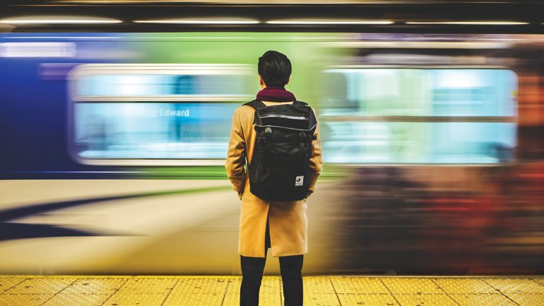 Man with backpack standing in front of colorful blurred speeding train.