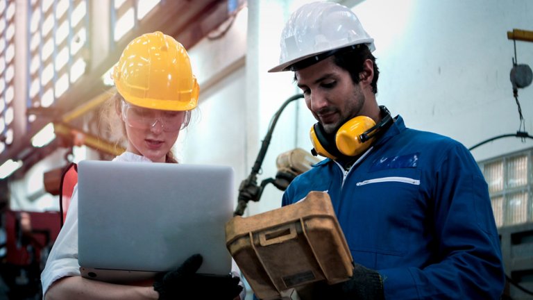 A woman wearing a hard hat holding a tablet with a man in a hard hat looking at the table