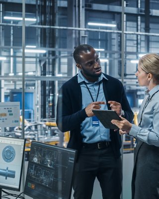 Female engineer using a laptop to consult with a colleague in an automotive plant control room