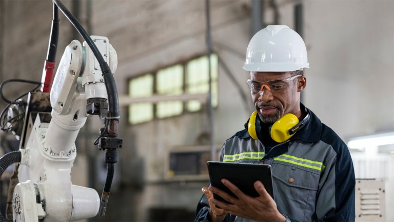 Male engineer wearing PPE and using tablet to monitor robot welding process in production line