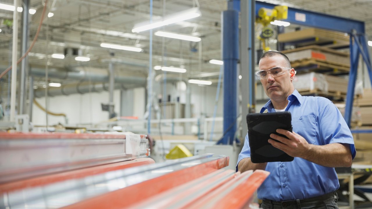 Man wearing safety glasses using tablet standing in front of packages and manufacturing facility.