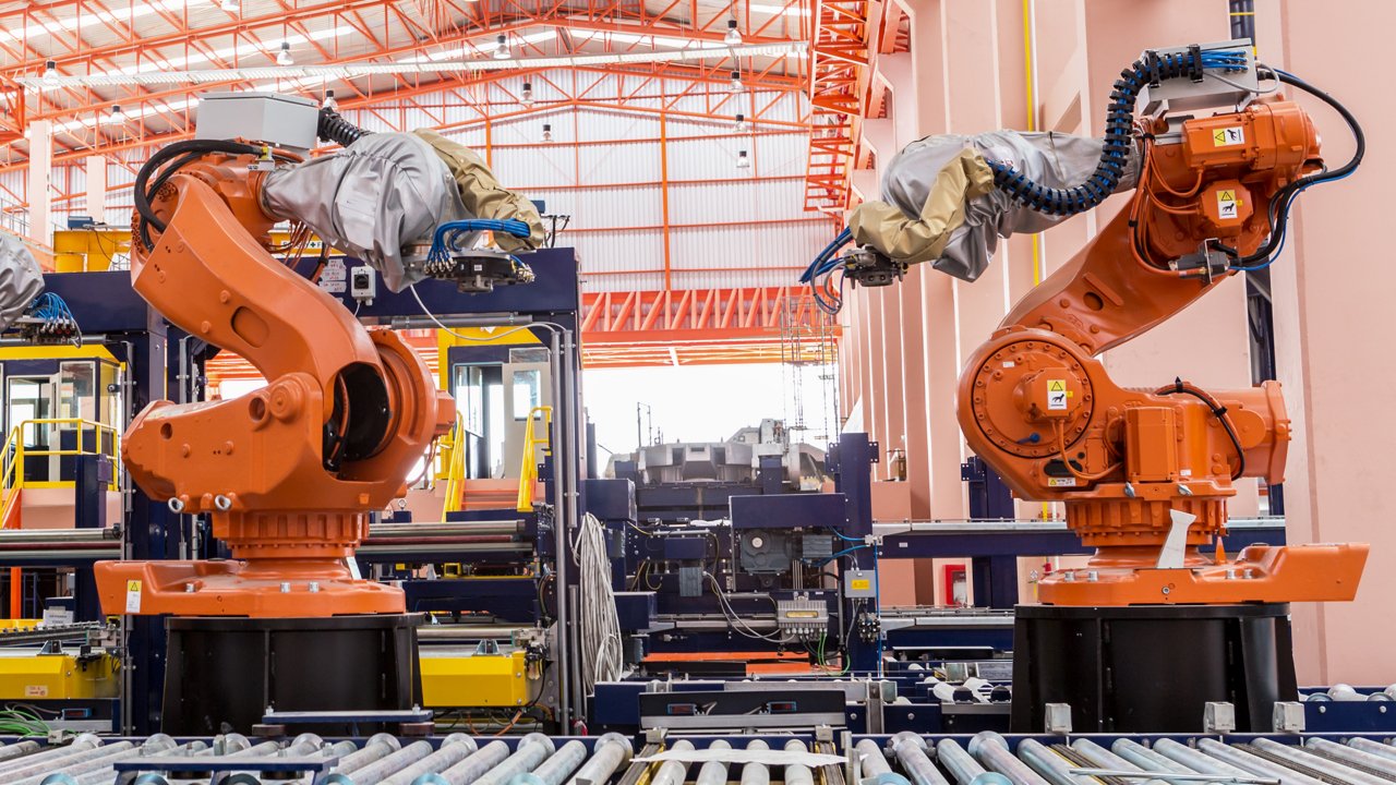 Deux immenses bras manipulateurs orange dans une ligne de fabrication en réseau cybersécurisé