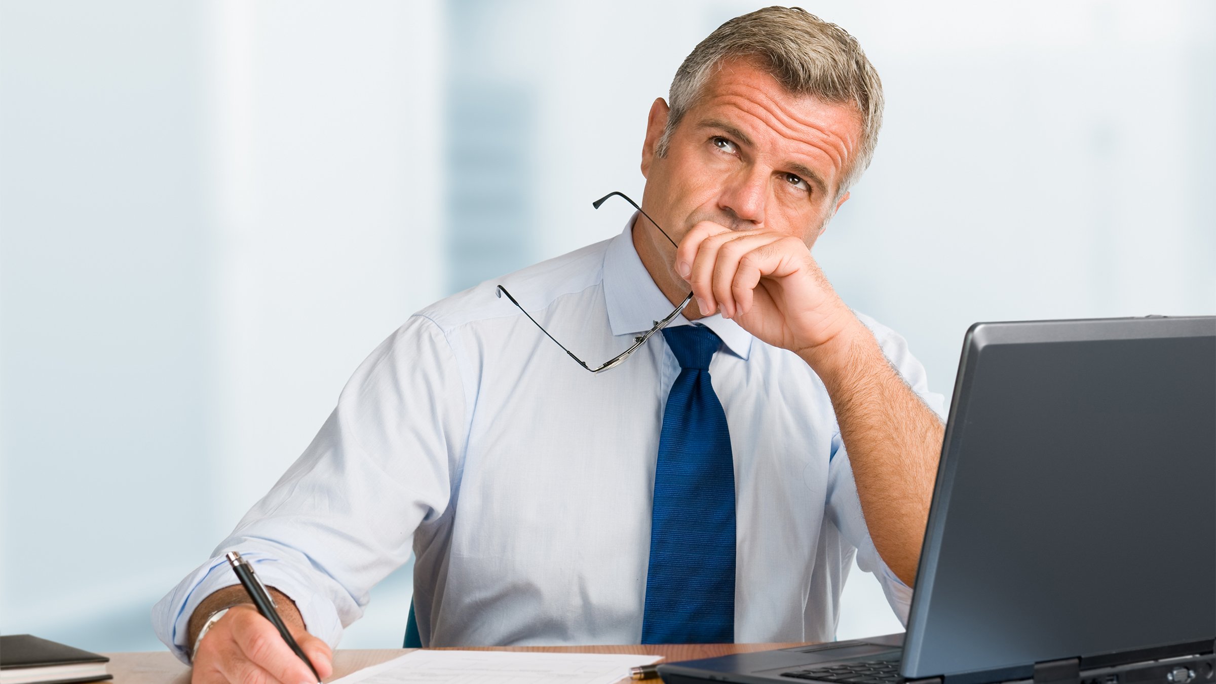 Pensive mature businessman looking up with concentration and writing paperwork in an office.