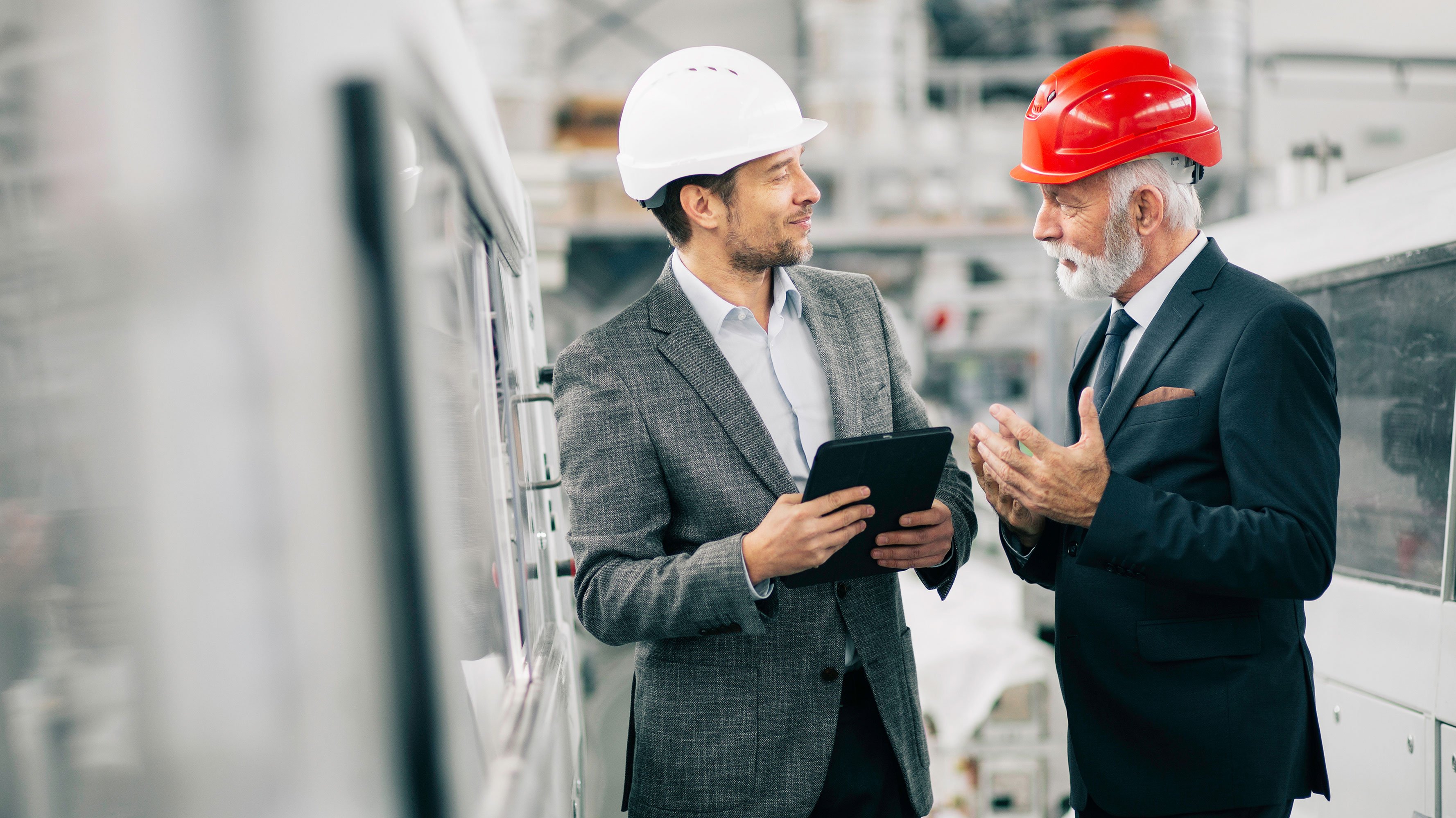 Men wear safety helmet and have a conversation in production area