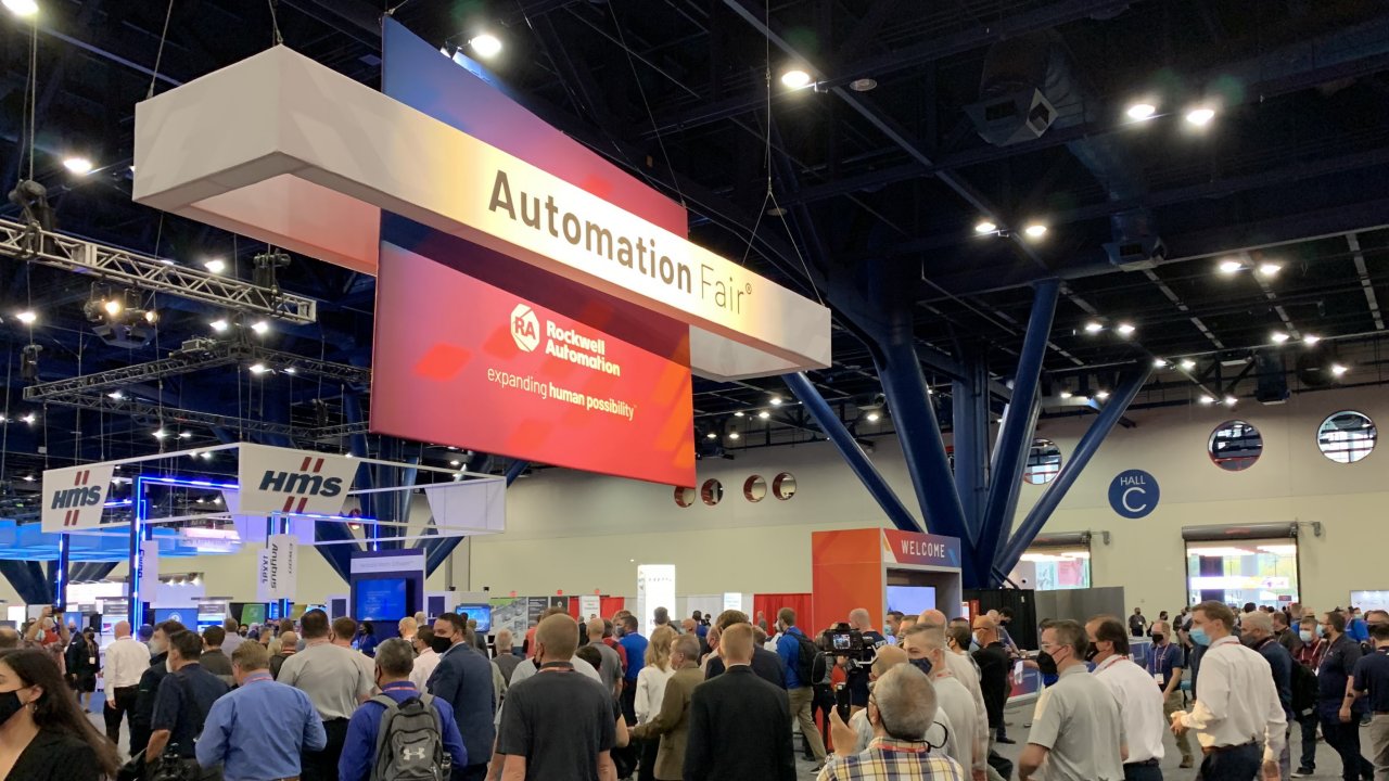 A crowd of people in a convention hall walk underneath a large Rockwell Automation banner at Automation Fair 2021 in Houston.