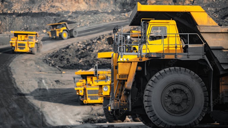 Five large yellow mining trucks are hauling coal or another black mineral mined from a pit quarry.