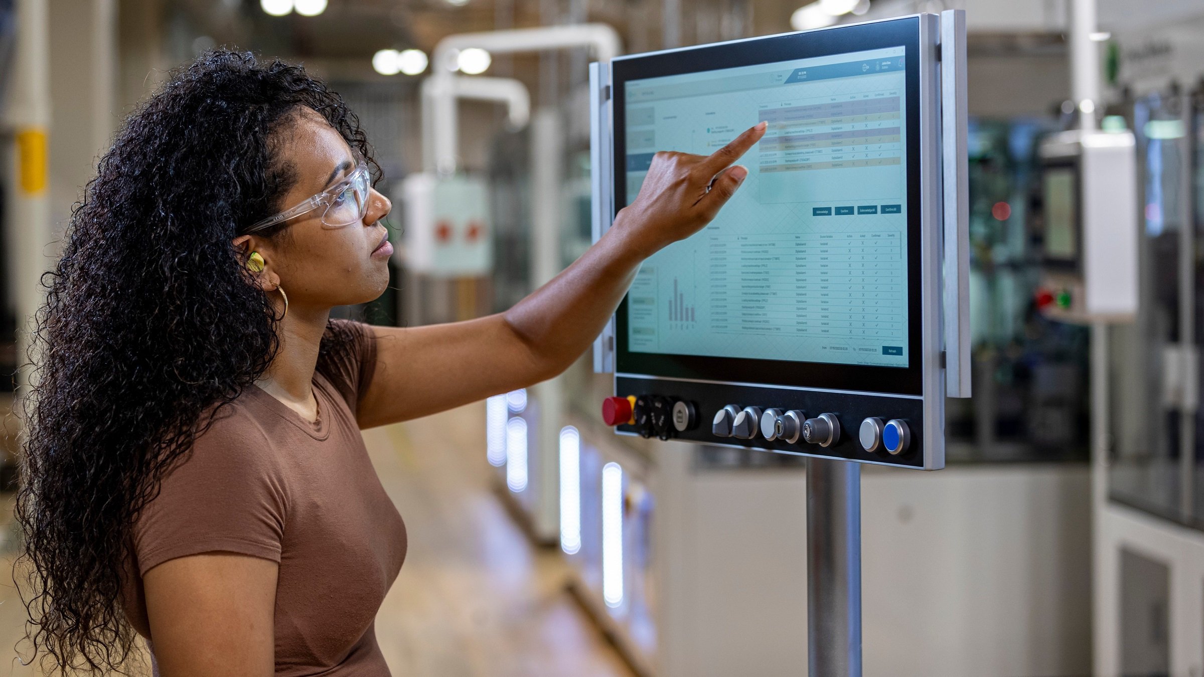 A woman in an industrial setting points at a computer screen, highlighting important information or data displayed.