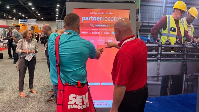 Two people in front of and pointing at PartnerLocator screen at expo show.