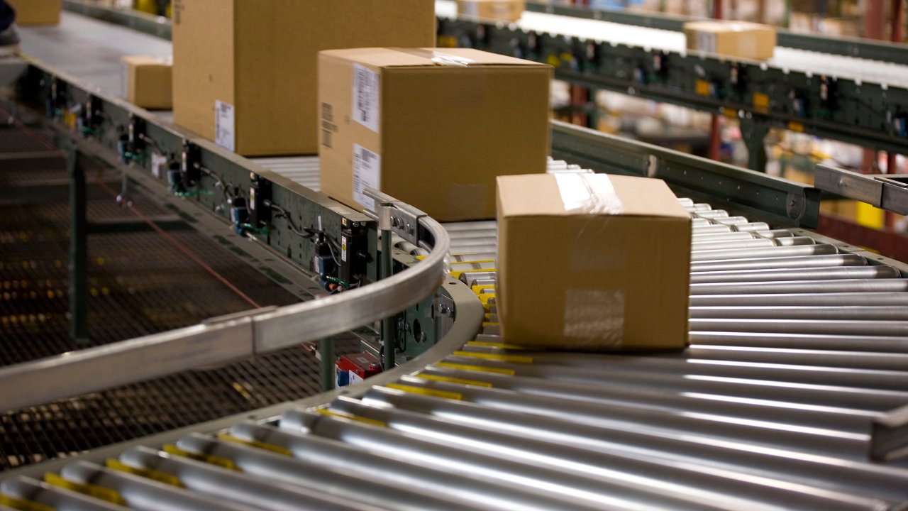 Packages in cardboard boxes being transported on a conveyor belt in a warehouse.