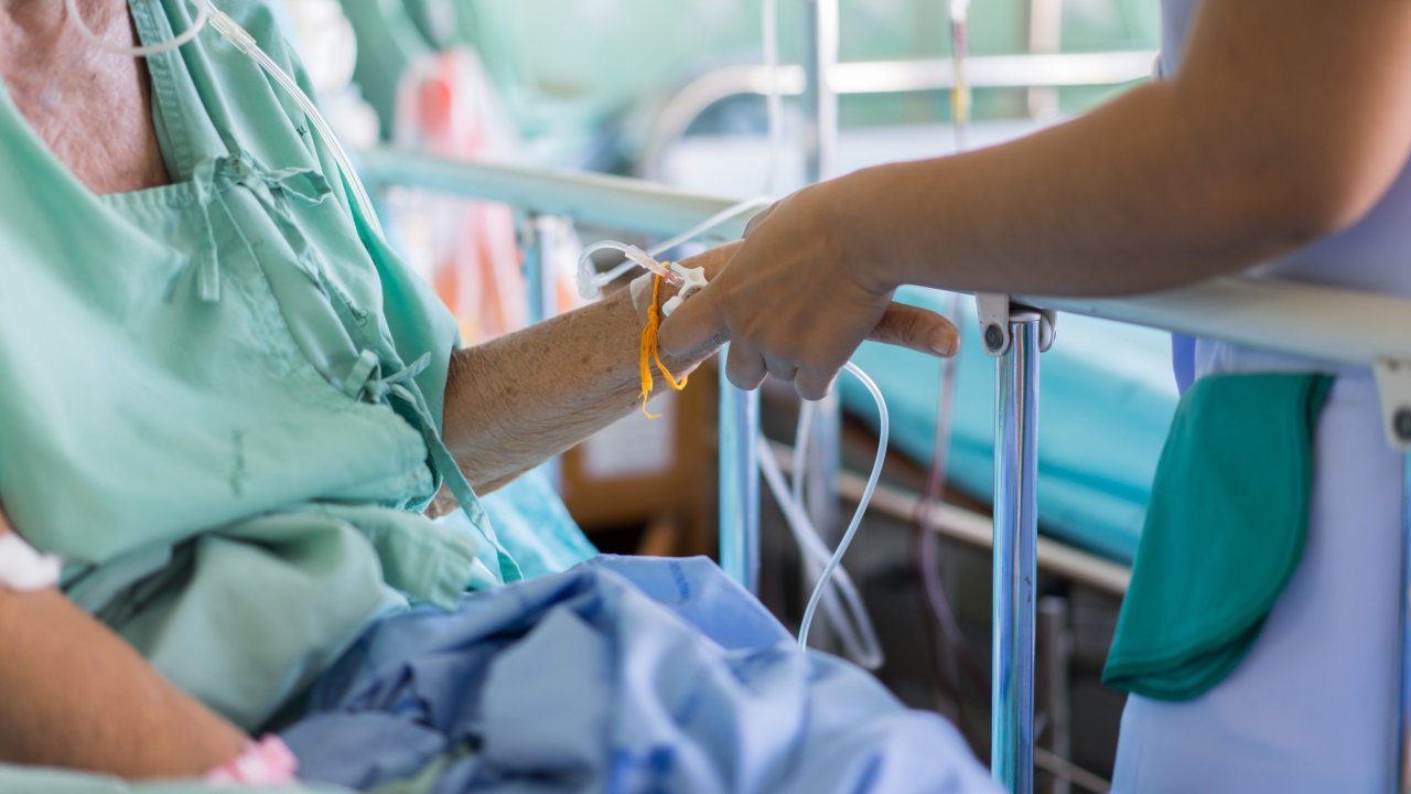 医院的一位医务人员站在一名老年病人的床边，将静脉留置针插到病人的手臂上。