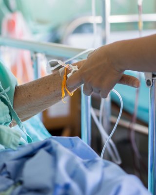 年配患者の病院ベッドの横で患者の腕への静脈内カテーテルの挿入を終える医療専門家。