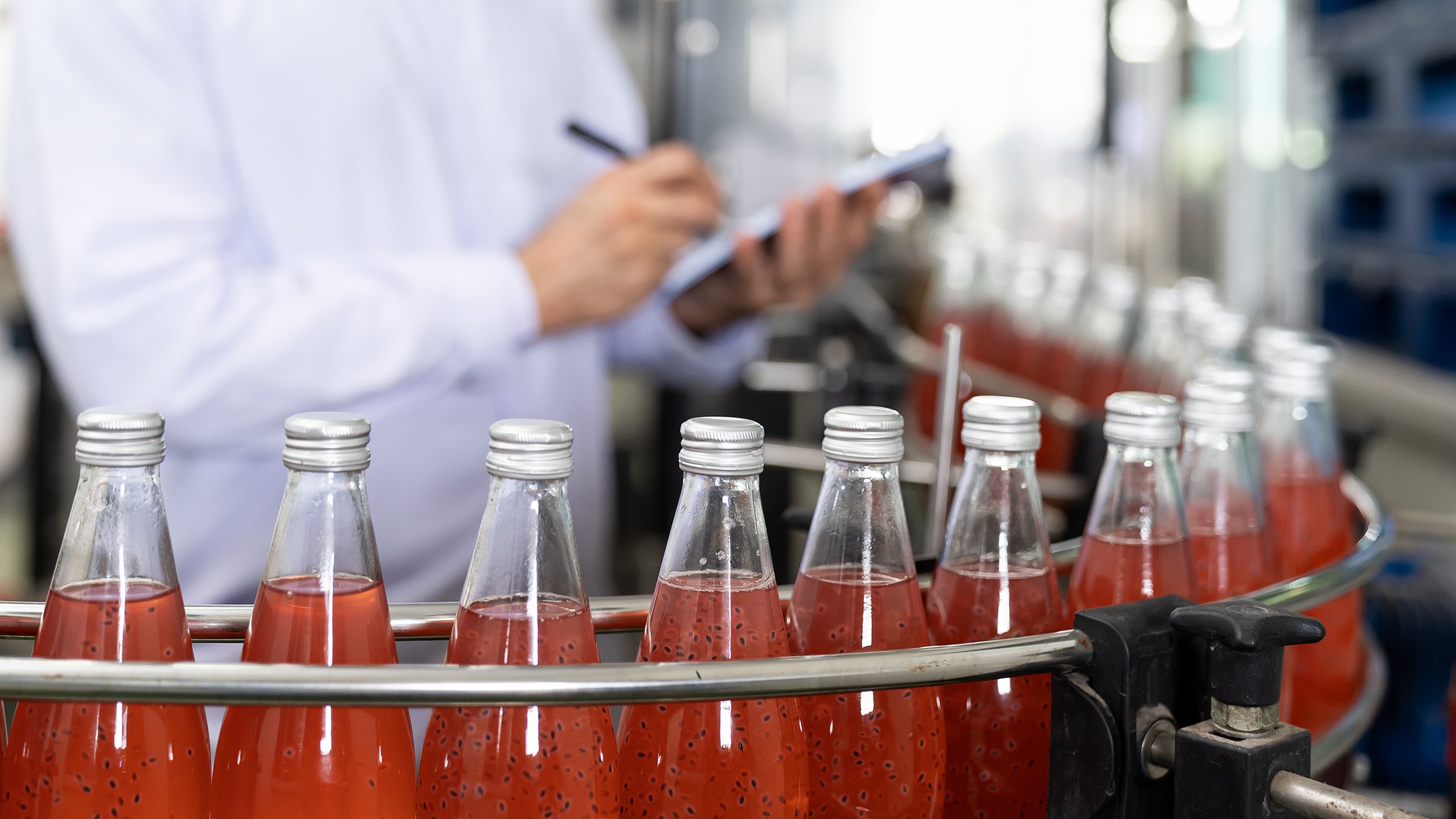 Male quality-control worker writing notes about Basil seed with fruit on beverage manufacturing bottling line.