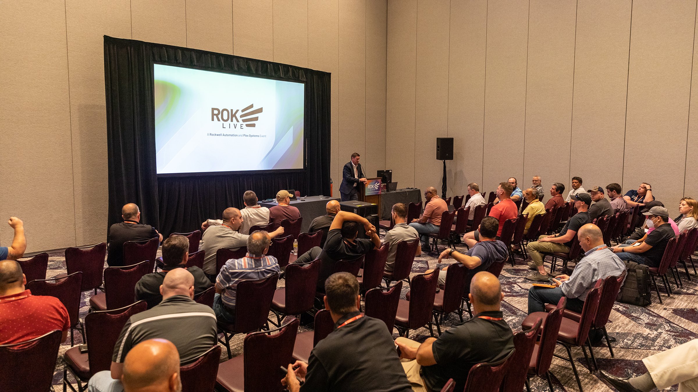 Room with many attendees listening to a speaker present in front of a screen at ROKLive 2022