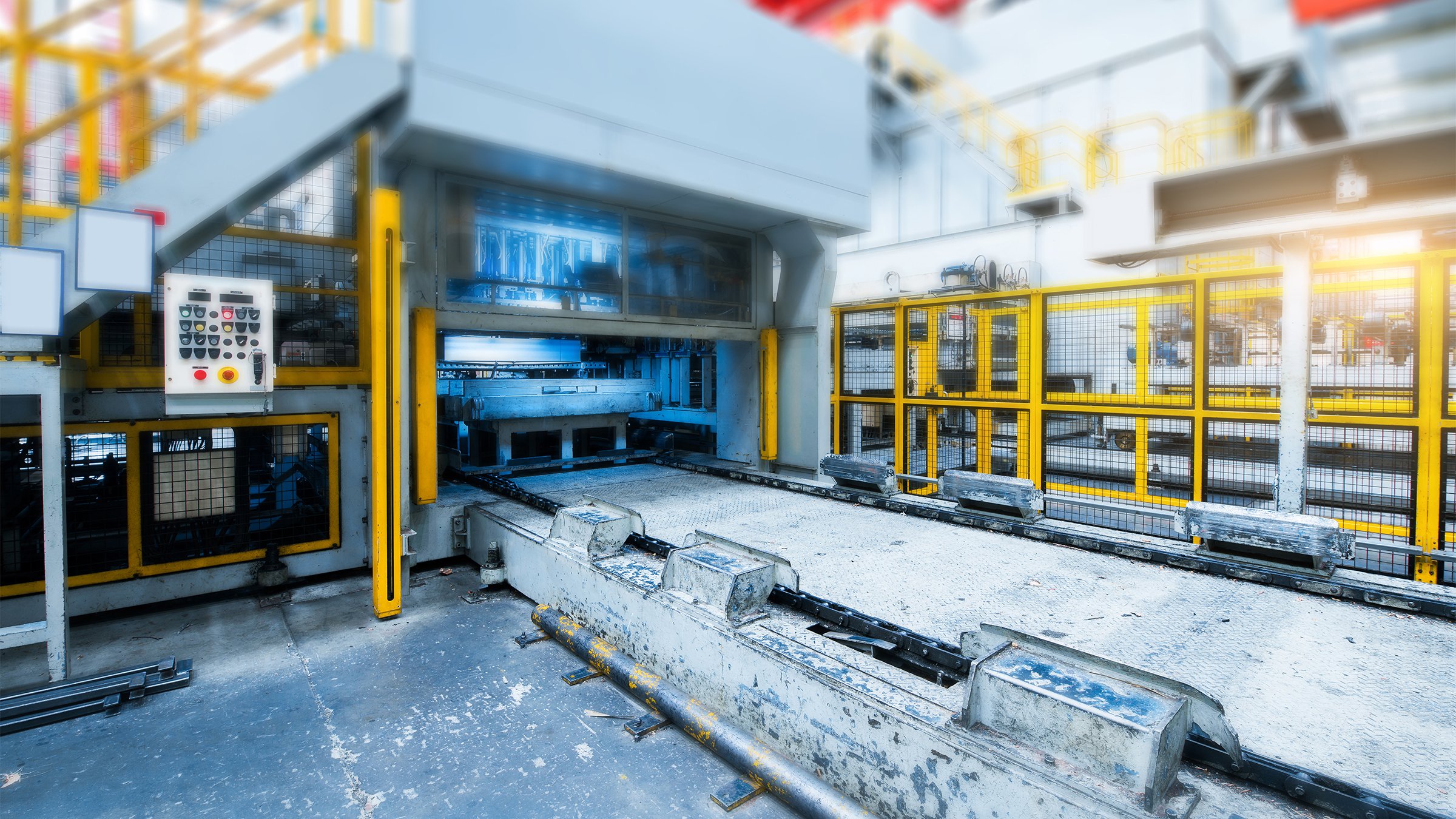 An industrial press machine in a factory with yellow safety guarding and light curtains surrounding it